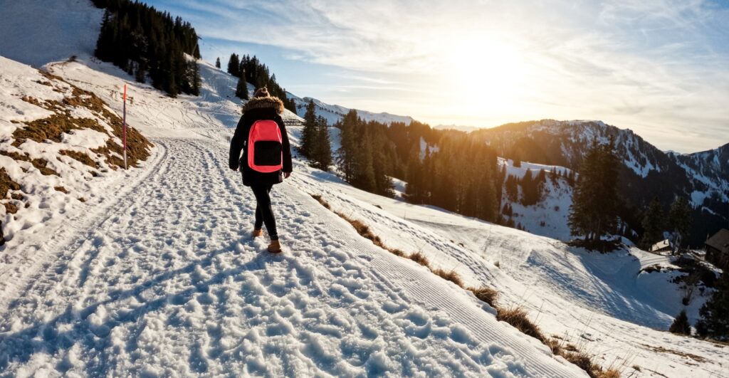 Young woman walking on snow mountain track during winter time at sunset